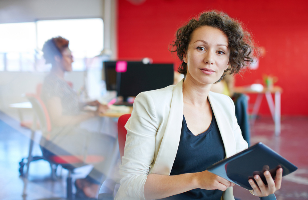 Confident female designer working on a digital tablet in red creative office space